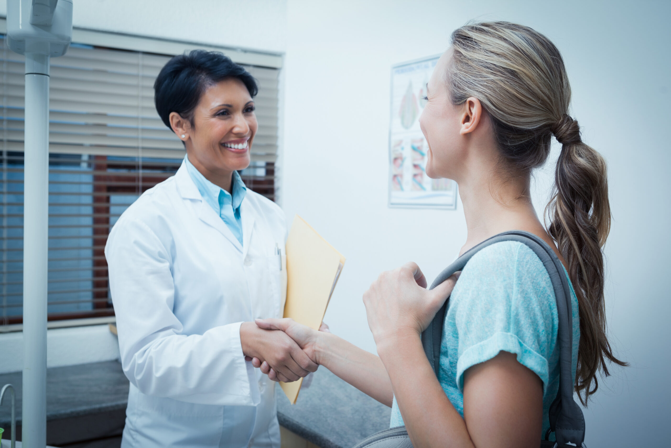 A doctor greets a patient with a handshake in a medical office, conveying a friendly and welcoming atmosphere.